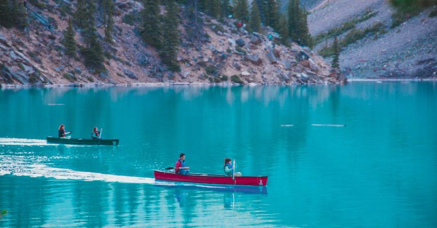 Kayaking Trip - Distant people in canoes on calm turquoise river surrounded by steep cliffs with green trees during trip in nature