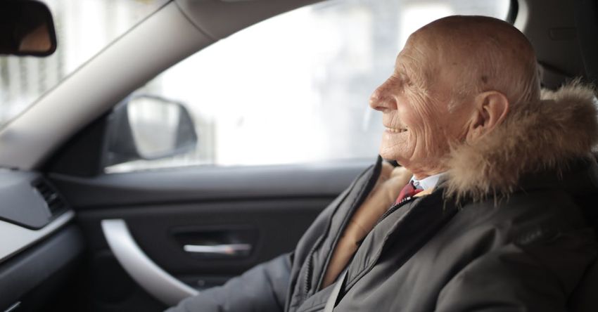 Travel Insurance - Side view of content elderly male in suit and outerwear sitting in front seat of contemporary automobile and looking away